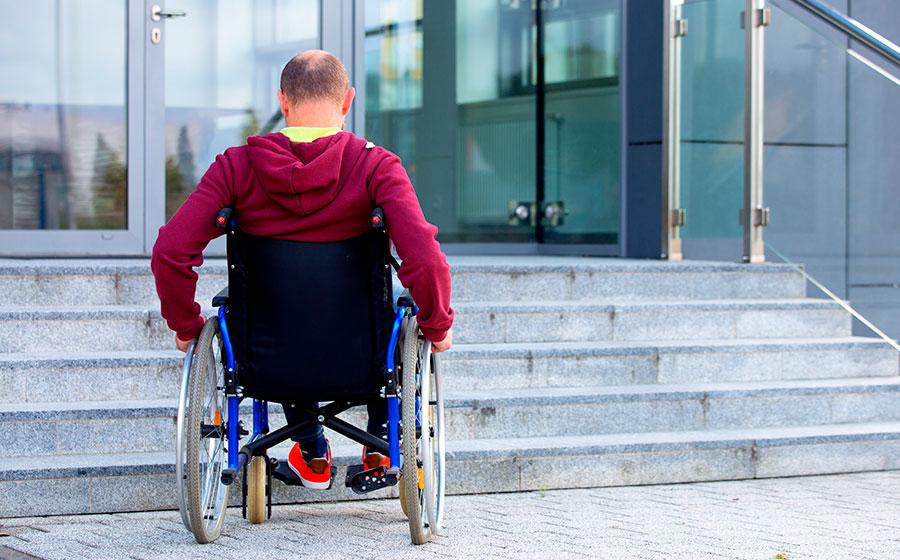 Un hombre en silla de ruedas frente a las escaleras de su edificio. | Foto: Apeyron
