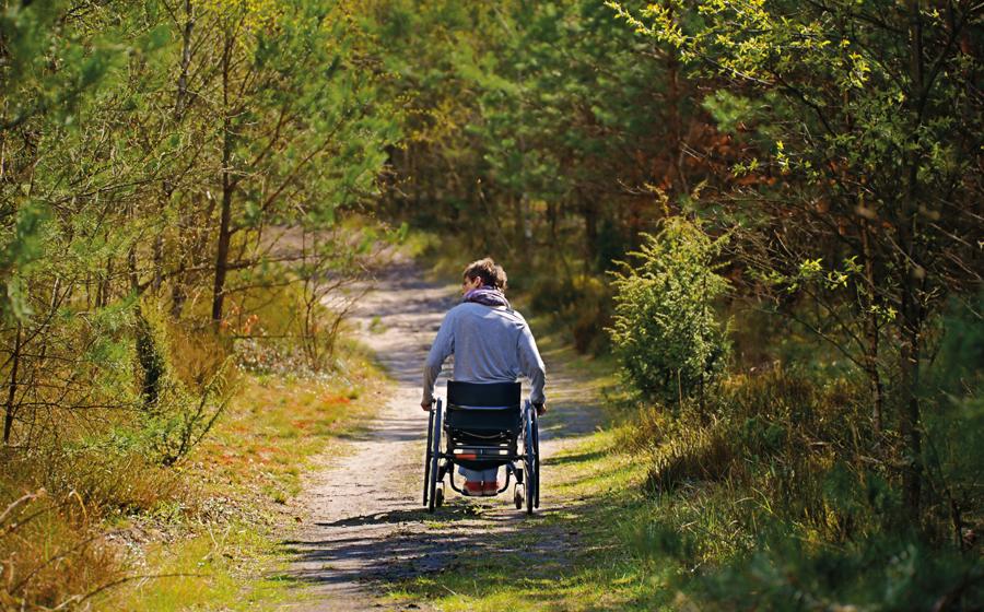 Una persona se desplaza en silla de ruedas por un camino sin asfaltar.
